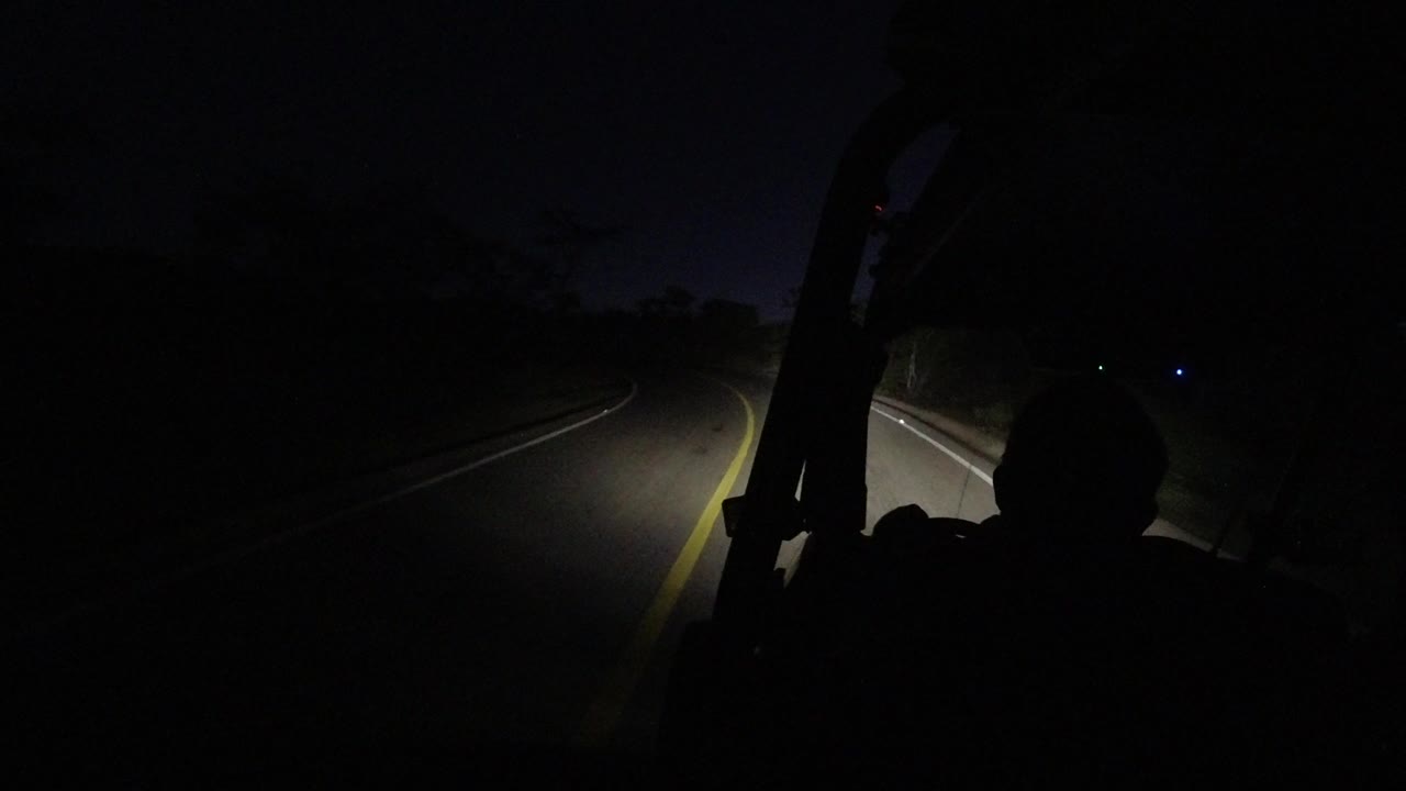 One second into the Los Cabos drive, the headlight beam falls across the right lane while the foreground person remains mostly in shadow.
