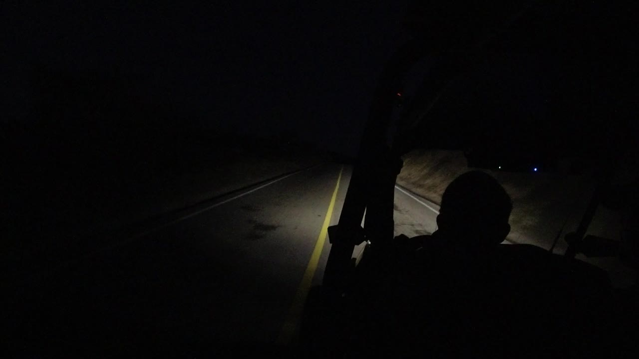 Dark road ahead with driver silhouette and headlight spill.