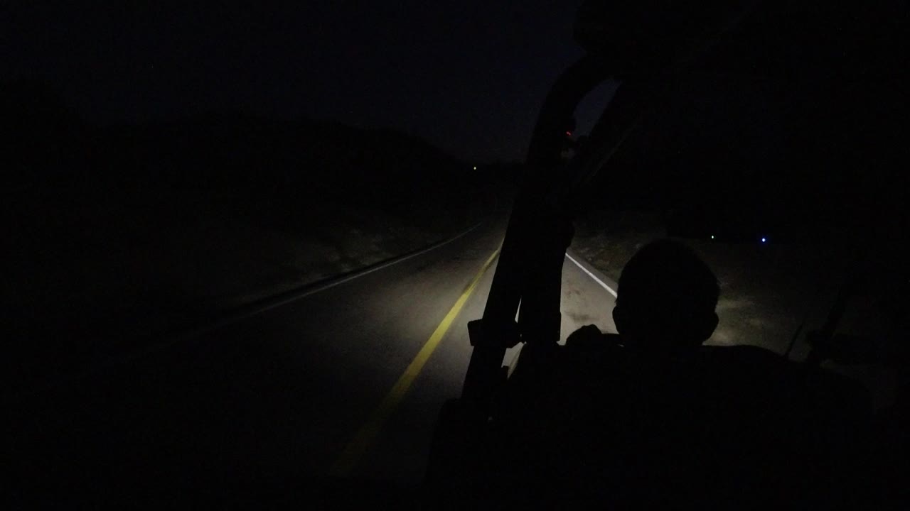 Dark road seen from a vehicle with headlights and a silhouetted person in front
