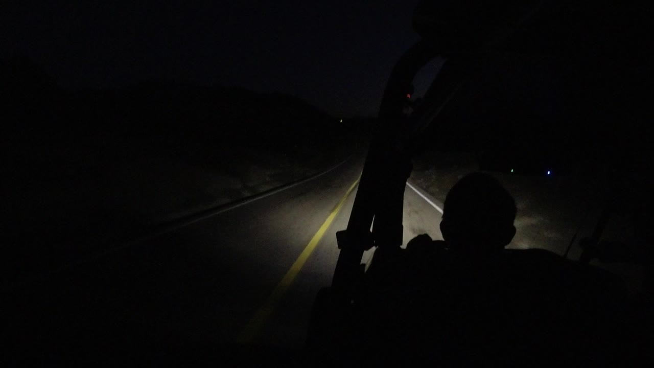 One second into the Los Cabos night drive, the headlight beam reaches farther along the pavement while the foreground passenger remains in silhouette.