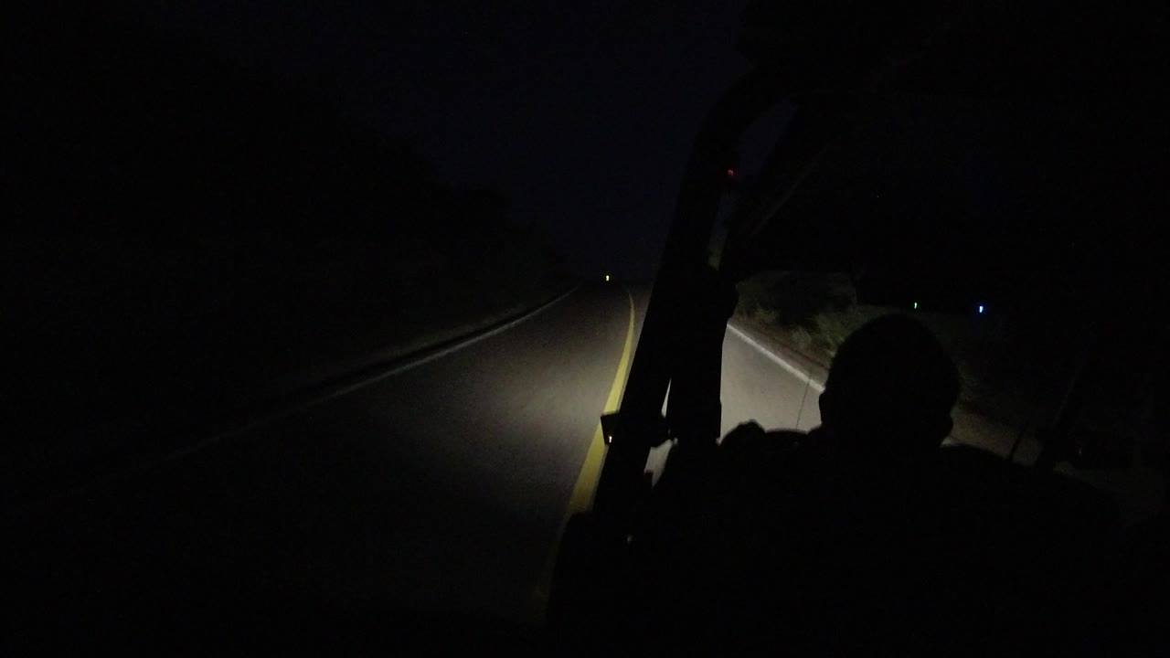 At 0:01 in Los Cabos, Mexico, the forward windshield view shows the driver silhouette lower in frame and the headlight beam stretching along the right side of the road.