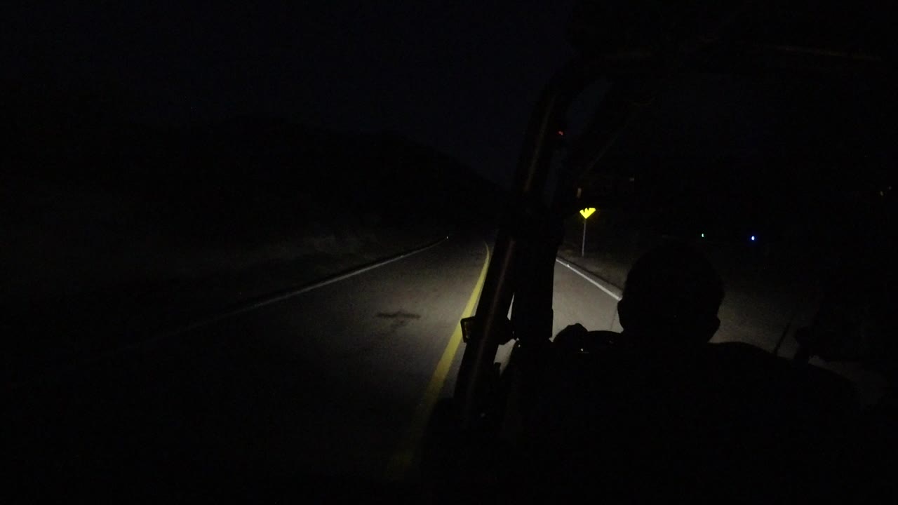 Dark bus windshield view of a narrow road lit by headlights