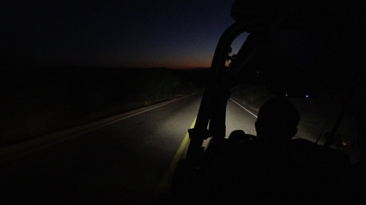 At 0:01, the headlight beam falls across the right side of the road in Los Cabos, with the windshield frame silhouetted and no recognizable faces visible.