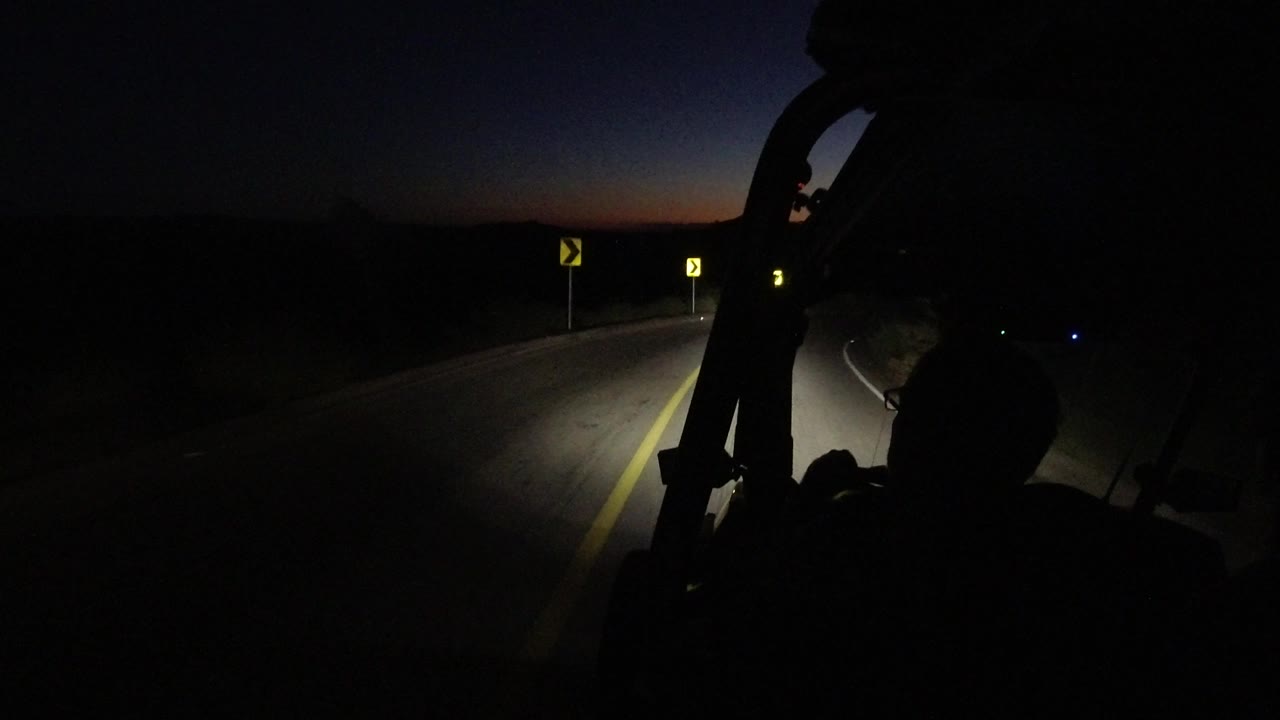 Open vehicle foreground with road signs on a dark curve.
