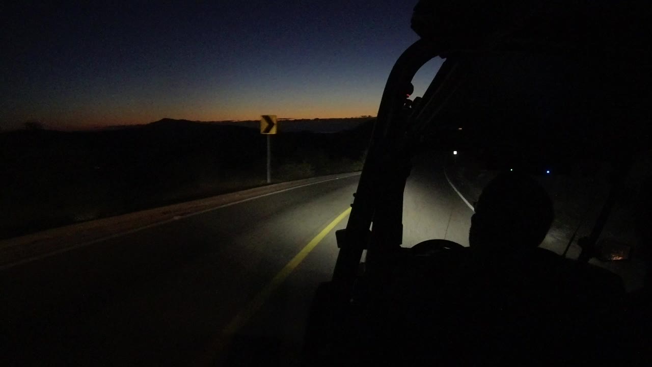 Dark car interior on a highway at dusk with headlights on the road.