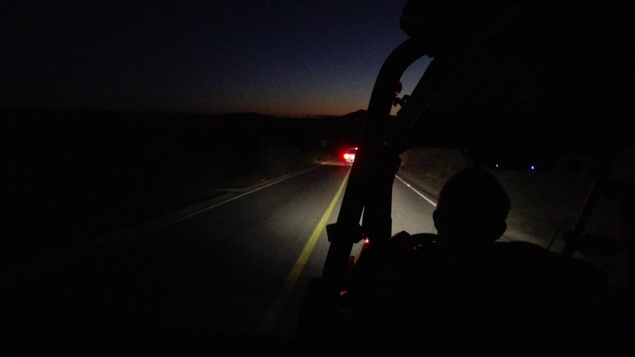 Dark road seen from inside a vehicle with silhouetted passengers.