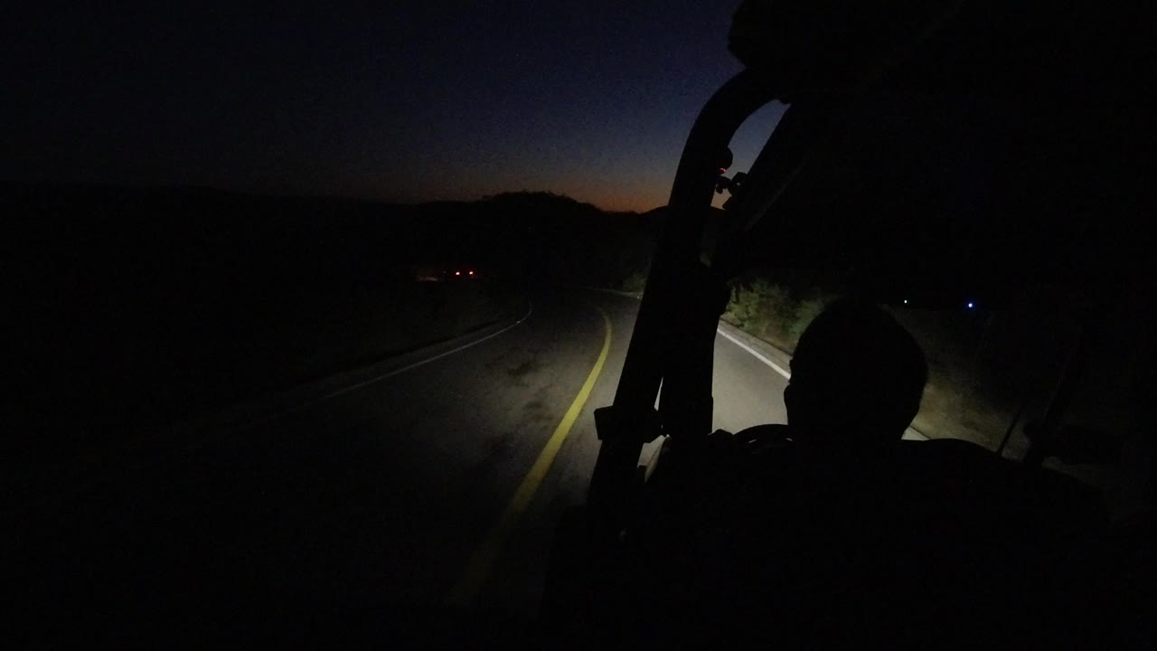 Dark road seen past a silhouetted driver and vehicle frame at night.