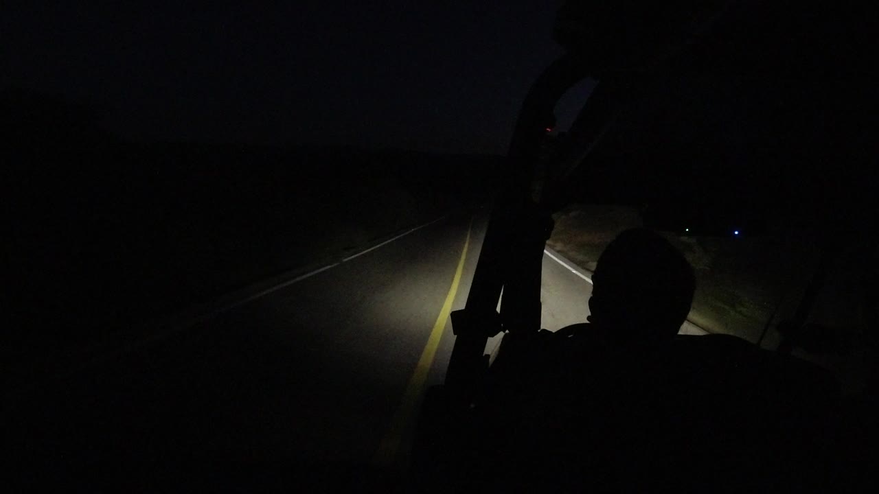 Dark jeep ride view with headlights on a road and a passenger silhouette.