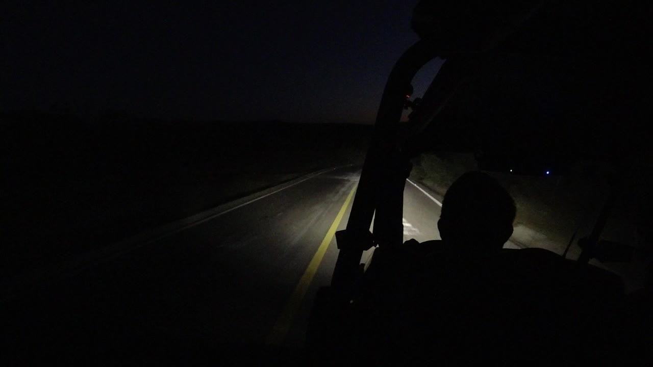 At the start of the Los Cabos clip, headlights illuminate a dark road and yellow centerline from behind an unrecognizable vehicle occupant silhouette.