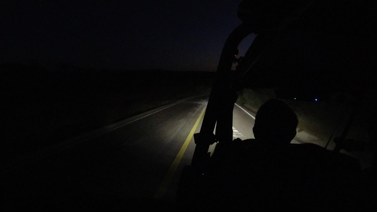 One second in, the Los Cabos road remains mostly black except for the headlight beam, the yellow line, and a dark occupant silhouette at the lower frame.