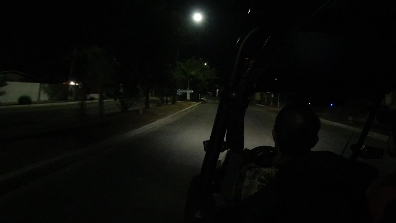 Opening view of a dark Los Cabos street from behind a vehicle frame, with the road lit by a bright forward spotlight and no recognizable faces visible.