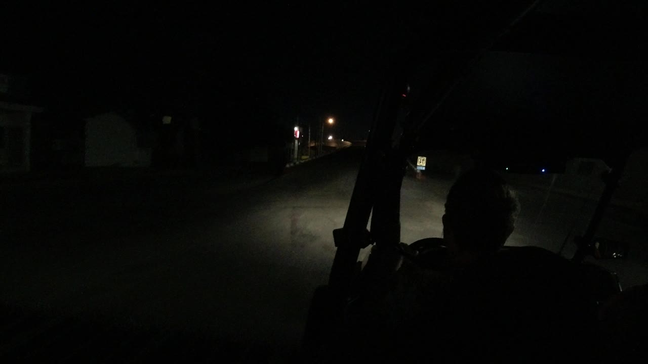 The road remains mostly empty in Los Cabos, with the driver silhouette low in frame and a small illuminated roadside sign ahead.