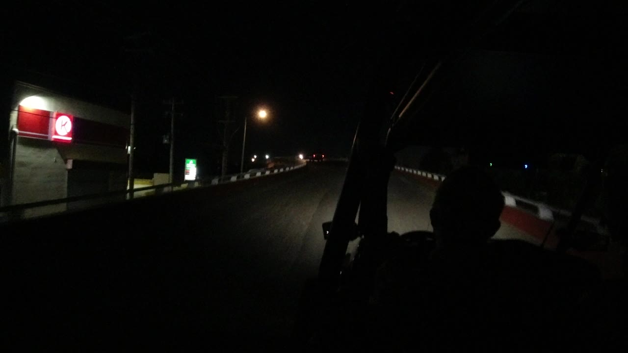 The Los Cabos road continues under sparse streetlights, with a red illuminated sign on a building to the left, a small green sign farther ahead, and no visible people.