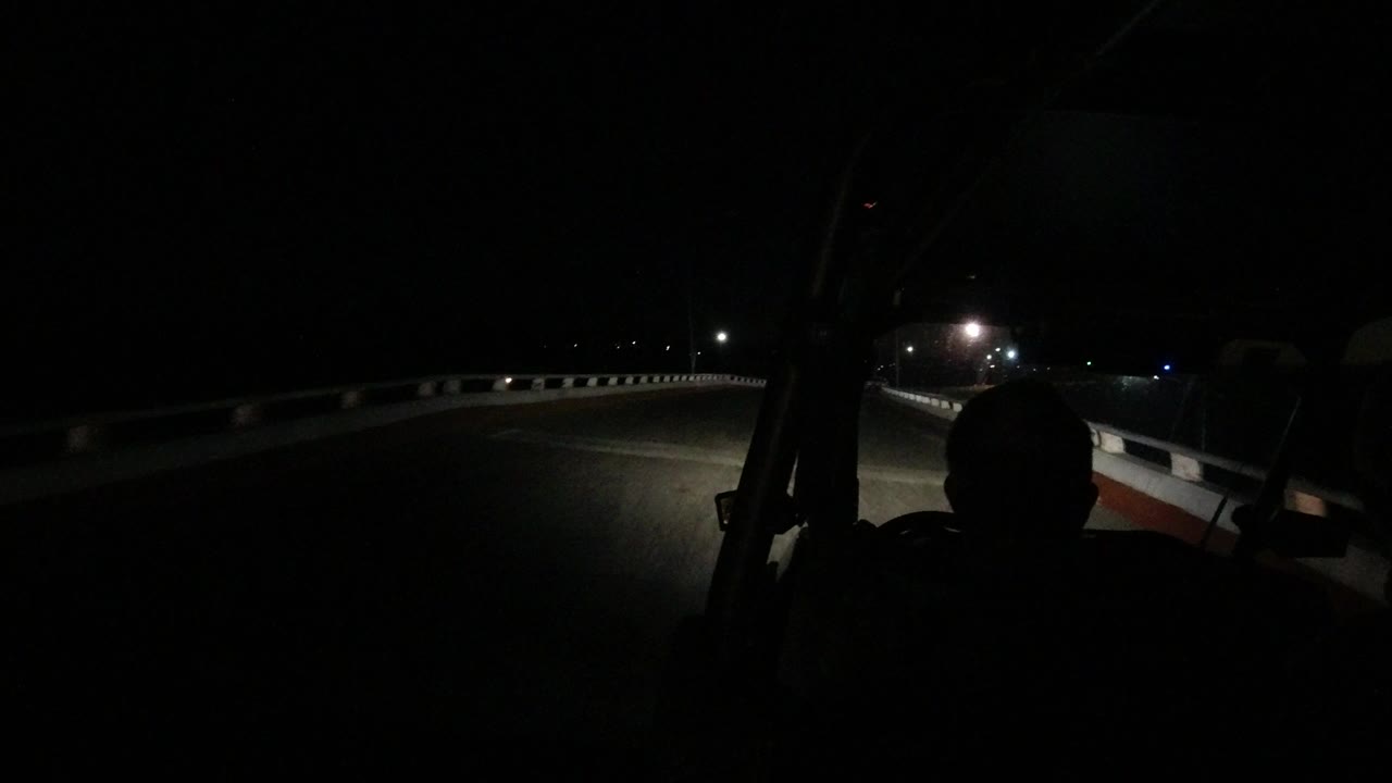 At the start of the Los Cabos night drive, headlights illuminate the bridge lane while a person appears as a dark foreground silhouette.