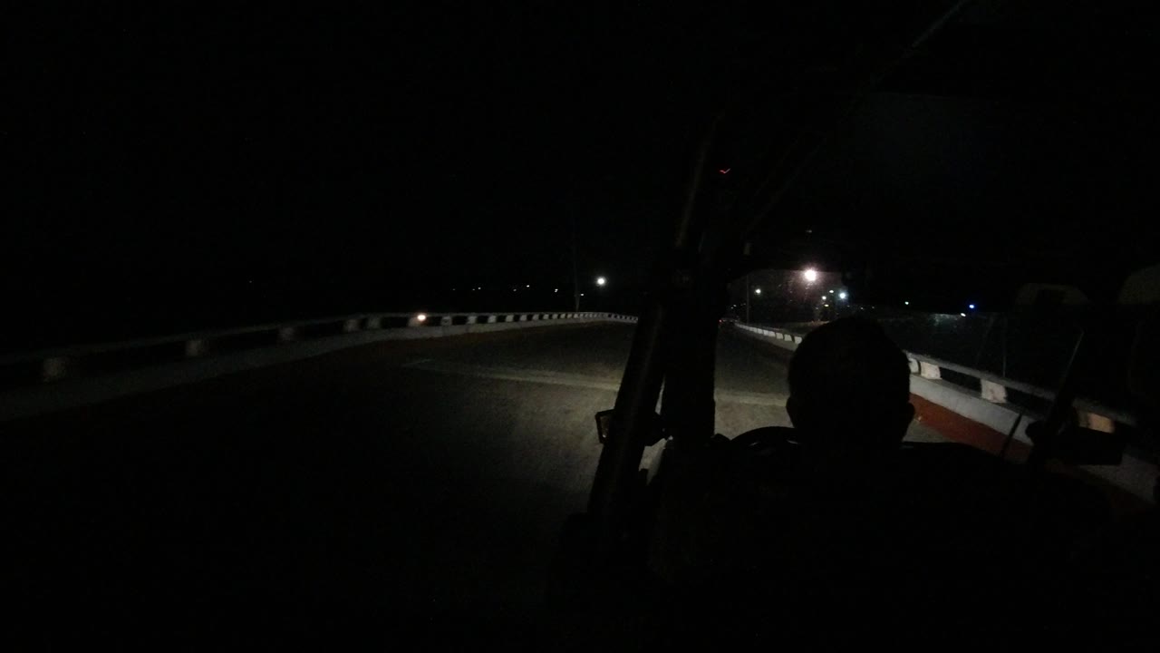 One second into the Los Cabos bridge drive, the headlight beam spreads across the road and the foreground person remains in silhouette.