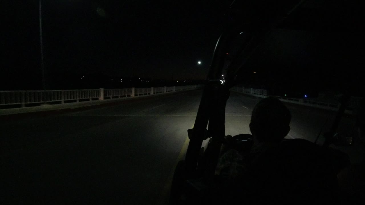 Dark road at night seen from behind a vehicle passenger silhouette.