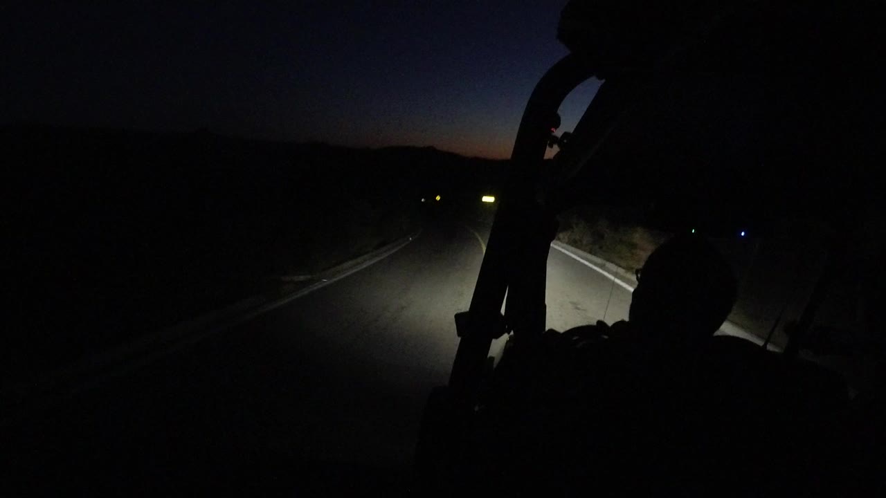 Dark road lit by headlights with a silhouetted person in the foreground.