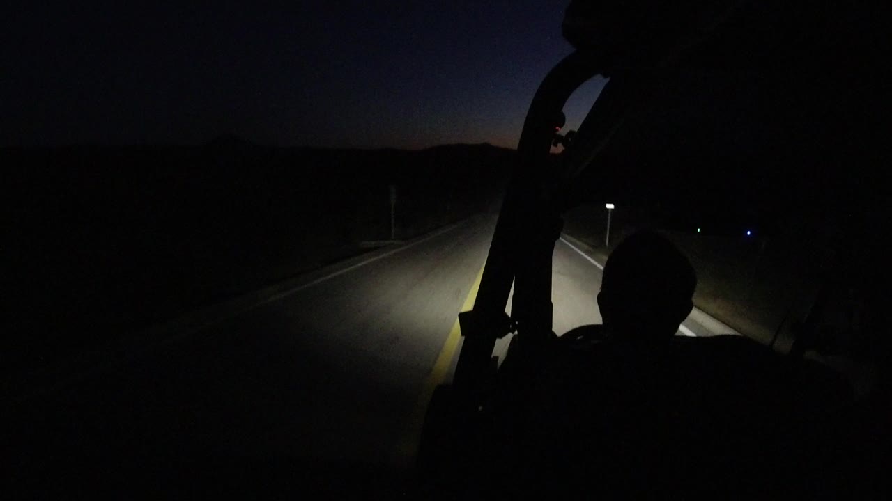 Dark road ahead lit by vehicle headlights at night.