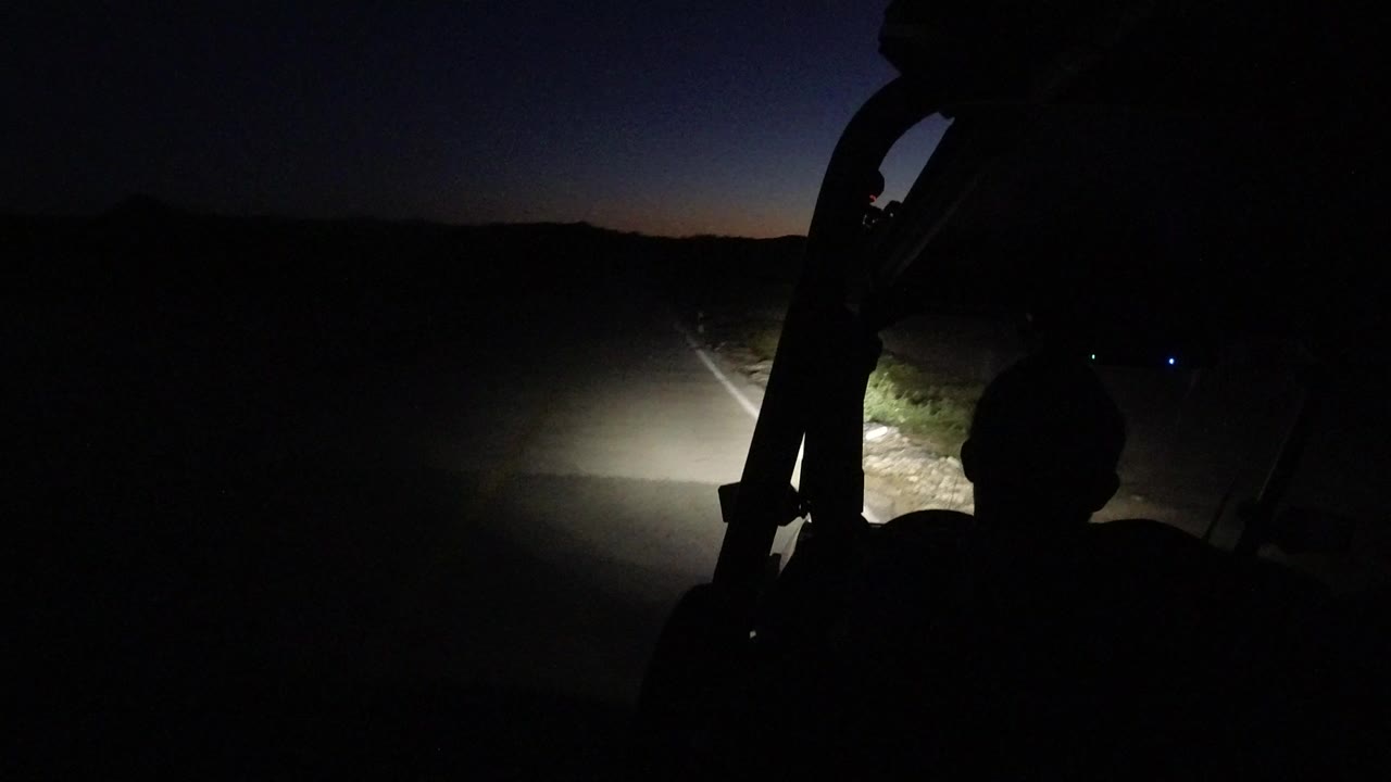 Dark jeep interior silhouette facing a headlit road before sunrise.