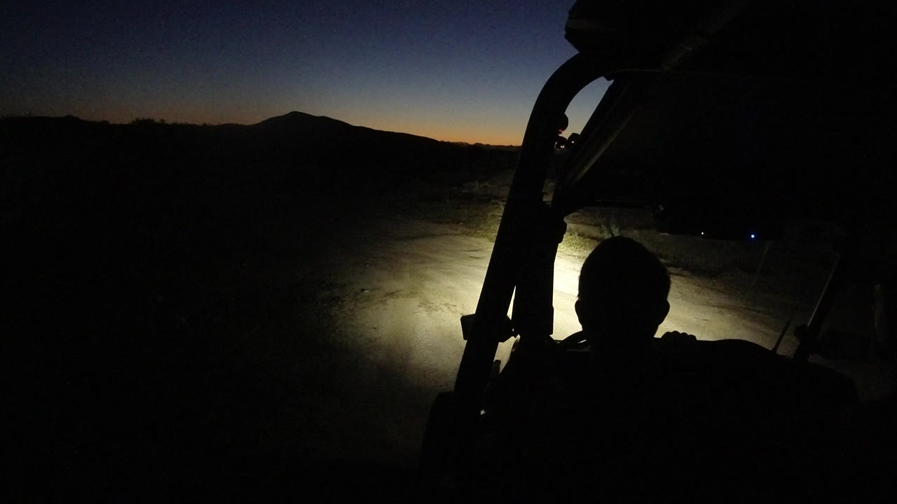Vehicle silhouette and headlight beam face a dark desert horizon.