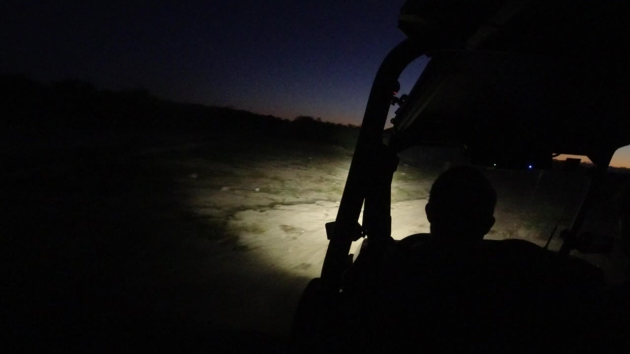 Dark vehicle interior facing a headlit dirt road at dawn