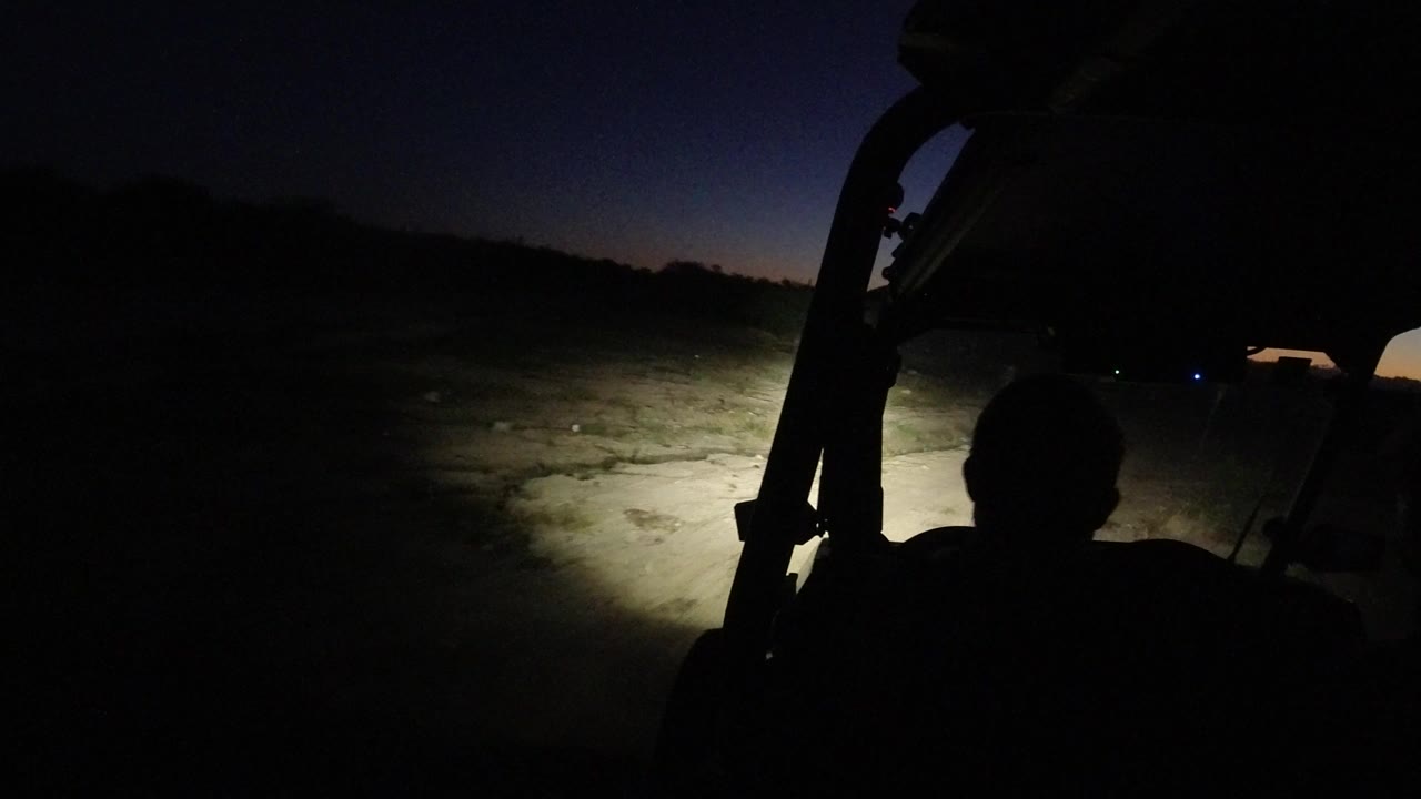 The Los Cabos road remains mostly dark as the headlights brighten a sandy patch ahead and the silhouetted occupant stays centered below the roof frame.