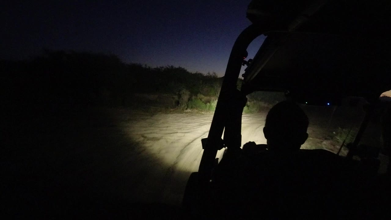 Silhouetted Jeep driver on a dark road lit by headlights.