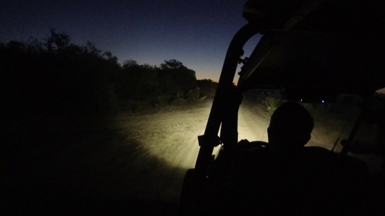 Dark vehicle interior facing a headlit dirt path at night.
