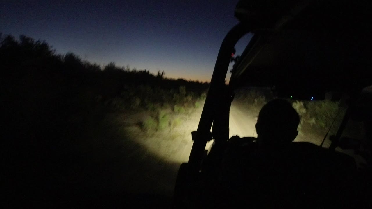 Dark vehicle view of headlights on a sandy road at dusk.
