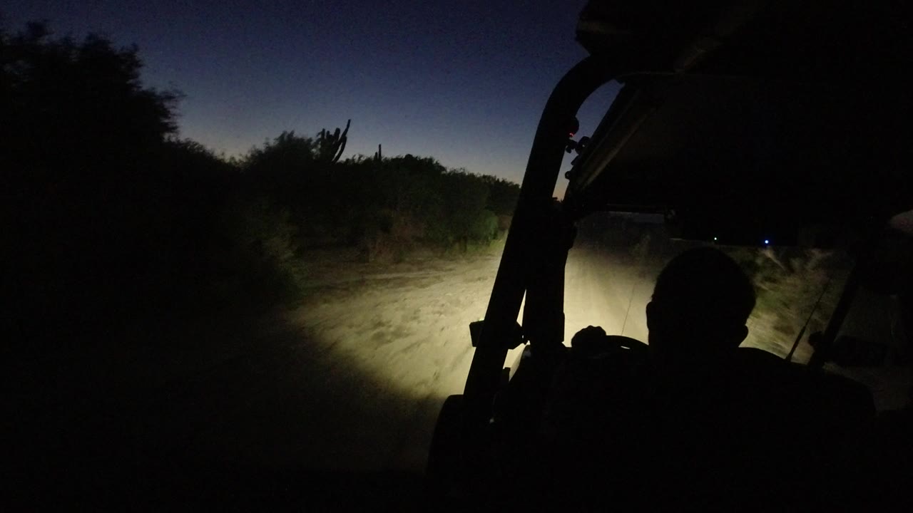 Vehicle silhouette and headlights on a curving dirt path at dusk.