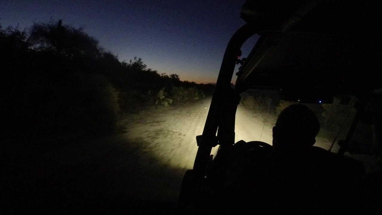 Jeep interior silhouette facing a headlit dirt road at night.