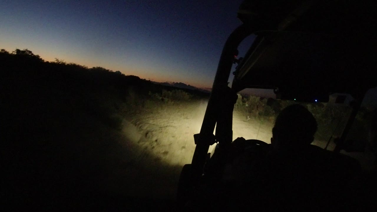 Dark jeep interior with headlights lighting a roadside path at dusk.