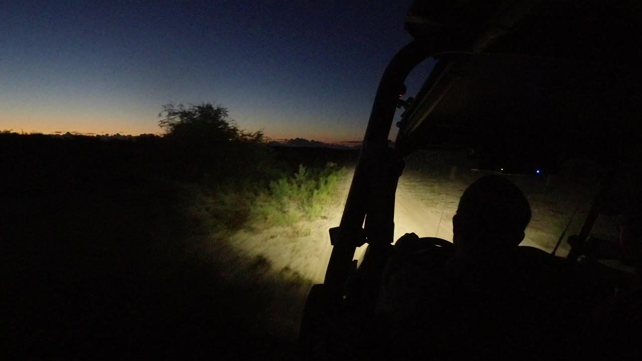 The off-road vehicle foreground stays dark while headlights pick out low desert vegetation and a narrow sandy path in Los Cabos, Mexico.