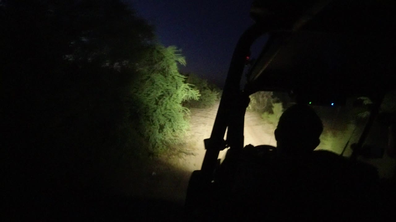 Dark vehicle silhouette facing a headlit desert track at night.