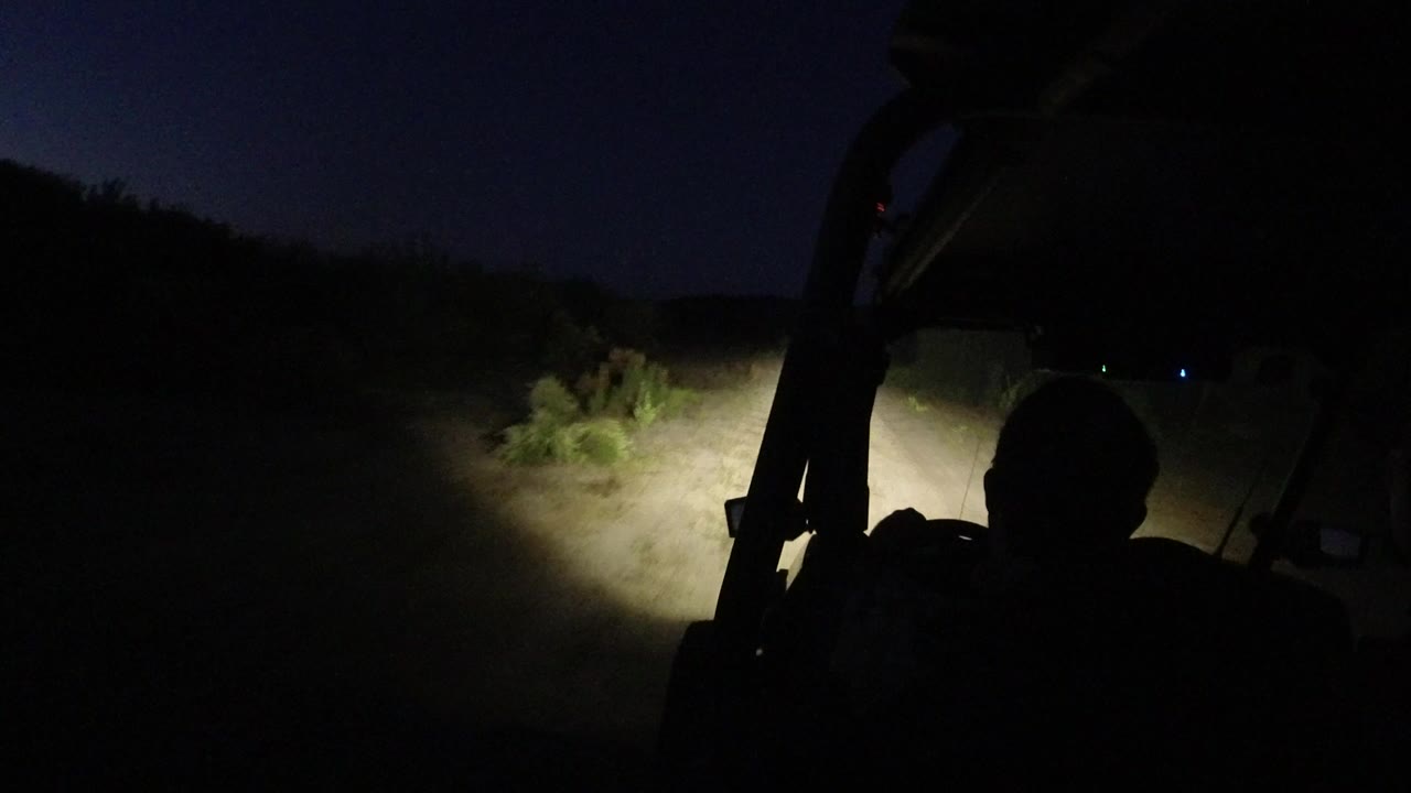 Headlights illuminate a dirt track from inside a dark off-road vehicle.