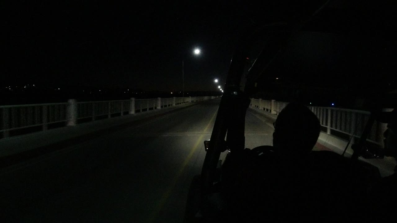 Start of the Los Cabos night road clip, looking forward along a dark two-lane roadway with guard rails, overhead lights, and no identifiable people visible.