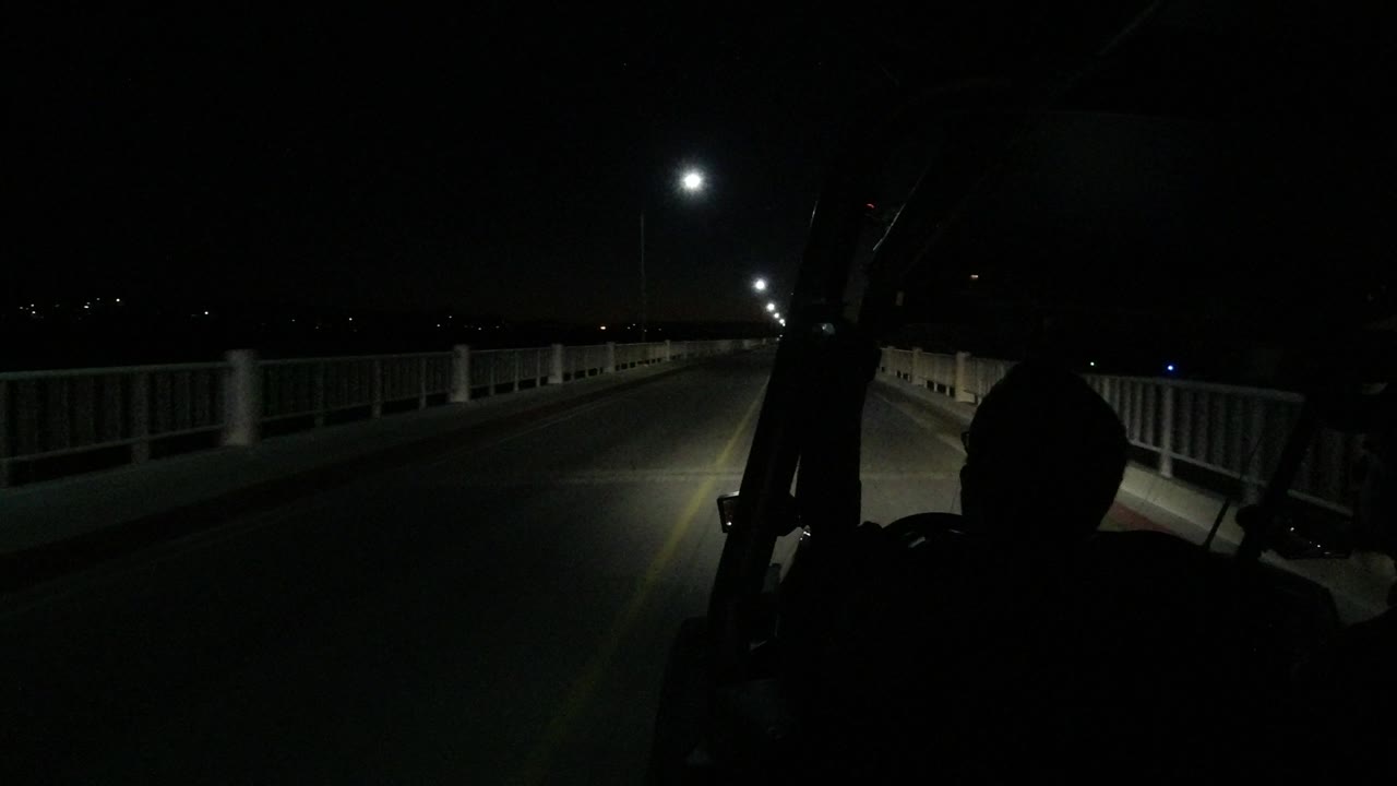 Los Cabos roadway at night with a bright streetlight ahead, guard rails running along the sides, and dark vehicle framing in the foreground with no identifiable people visible.