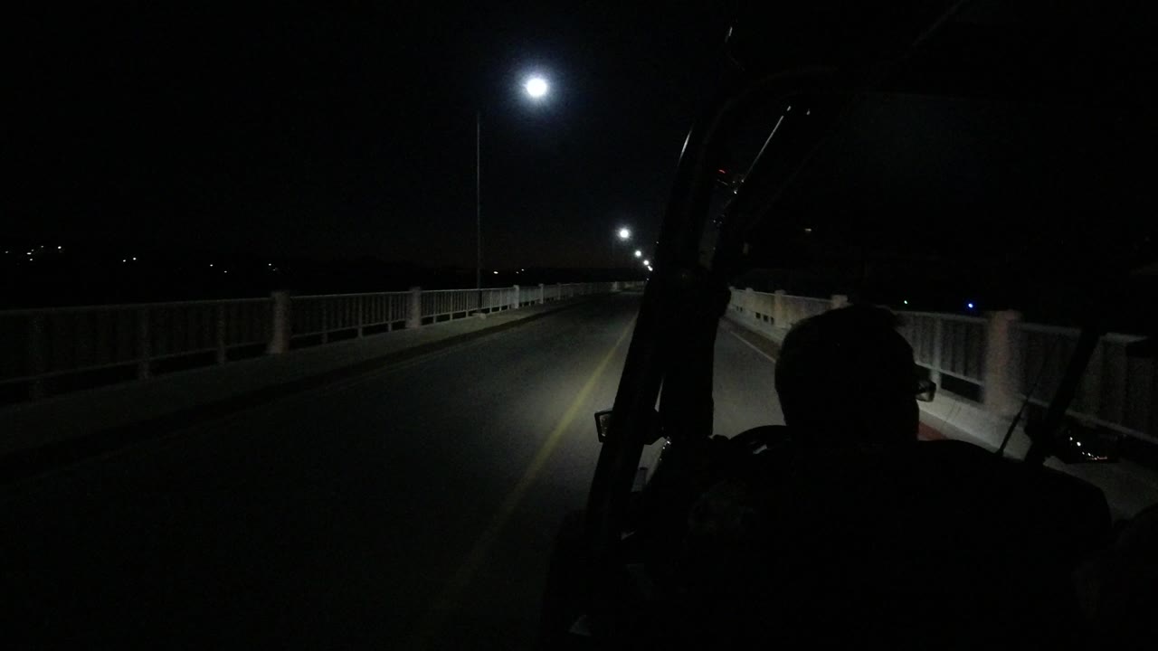 At 0:01, the Jeep continues along the Los Cabos bridge, with the passenger silhouettes darker against the lit lane and railings fading into the night.