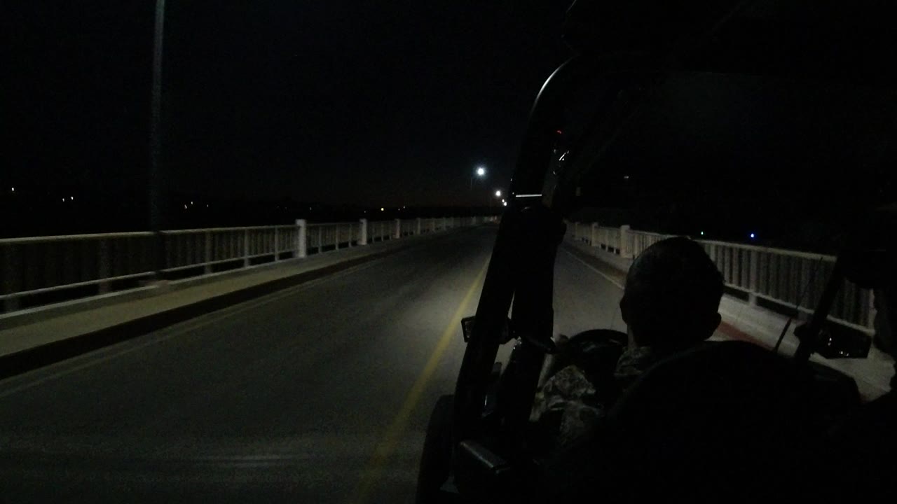 Dark vehicle view along a bridge road at night with a silhouetted passenger.
