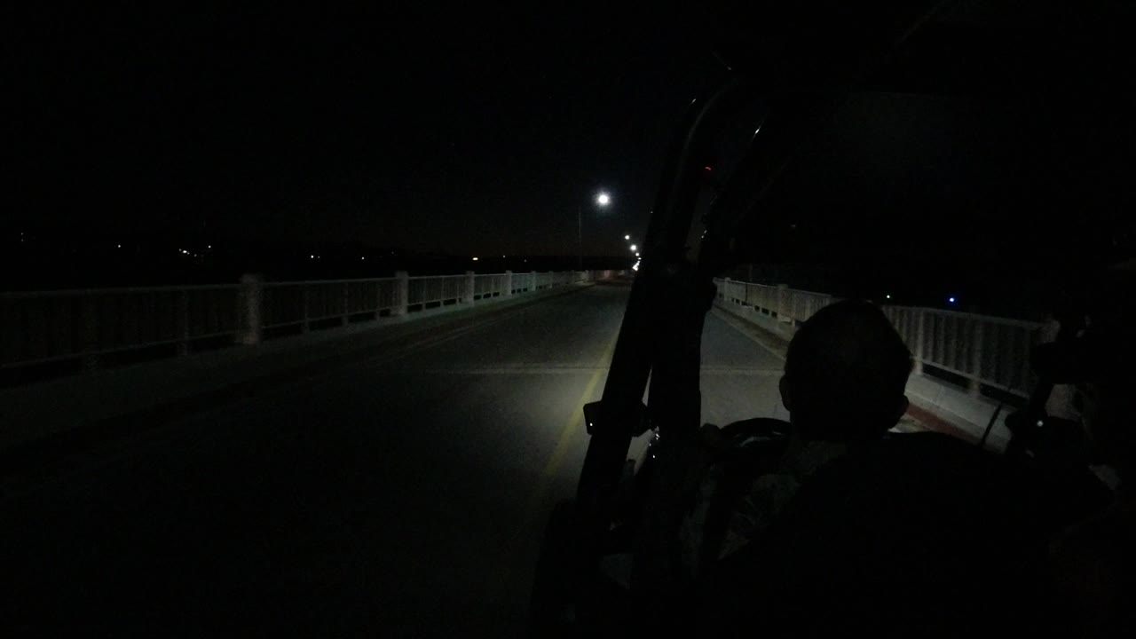 Dark road ahead with jeep headlights and roadside railings at night.