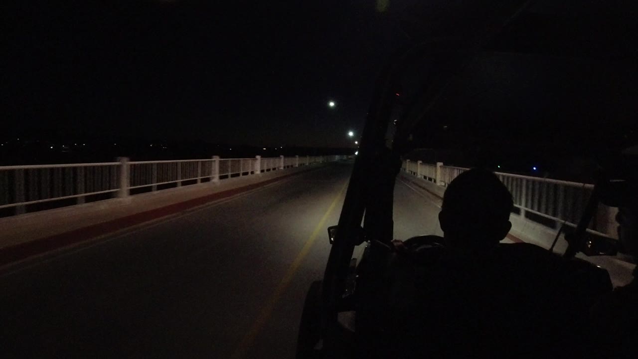 A second into the Los Cabos drive, the road remains centered between white railings while headlights illuminate the pavement and distant darkness.