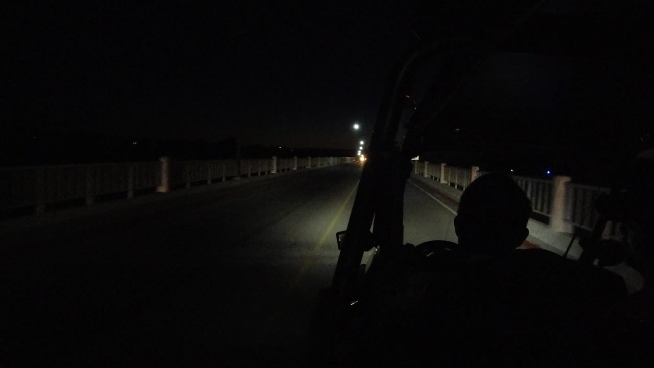 Night road with a center line, side railings, and a dark foreground silhouette.