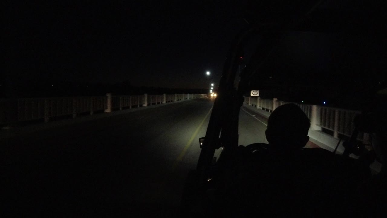 A low-light Los Cabos road view shows railings on both sides, a small roadside sign, and the black outline of a rider beneath the vehicle structure.