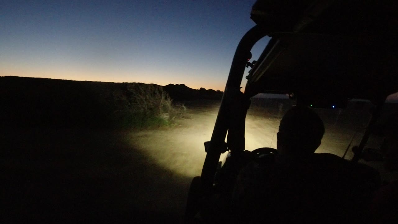 One second into the Los Cabos, Mexico ride, the vehicle frame and a rider silhouette remain in the foreground as the headlights spread across roadside brush and airborne dust.