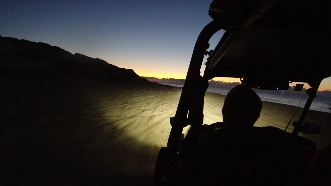 Vehicle interior silhouette facing a dark beach at sunset