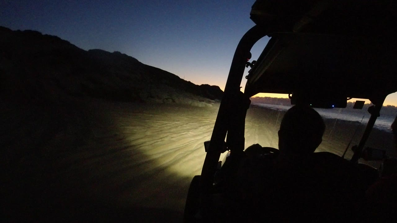 At 0:01 in Los Cabos, Mexico, the headlight beam reaches farther across the dirt road while the driver's head remains centered in silhouette against the dark vehicle frame.