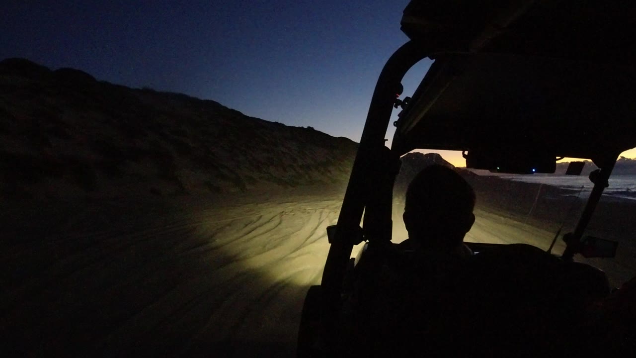 Open-roof vehicle interior at dusk with headlights on a dirt road.
