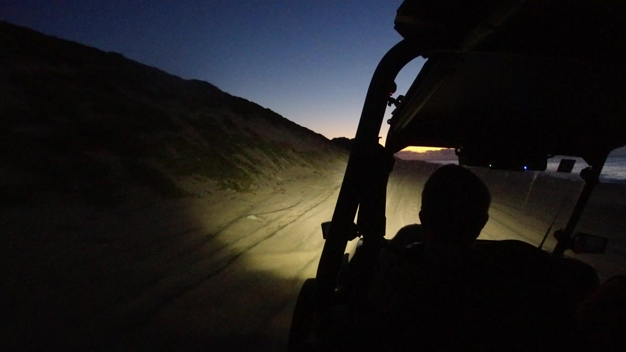 Headlights illuminate a rough road with a driver silhouette in the foreground.