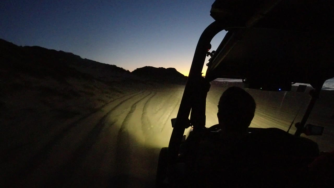 Dark off-road vehicle interior looking toward headlights on a sandy desert road.