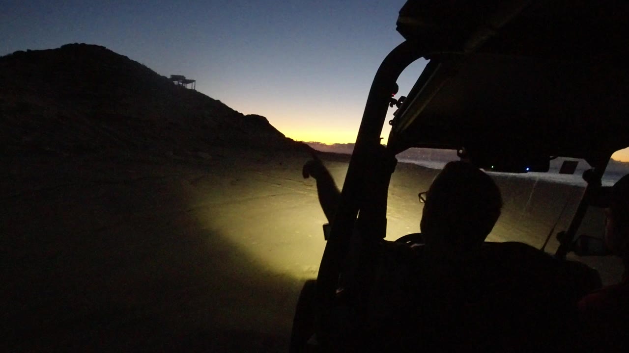 Golf cart silhouette facing a headlit dirt road at dusk.